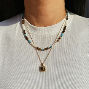 Detail of layered necklace featuring brown tiger eye beads and vintage square gold pendant