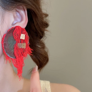 Close-up of bohemian large red fringe earrings with gold metal accents on a model