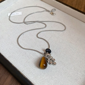 Detailed shot of tiger eye pendant and silver tassels on a sleek box chain necklace