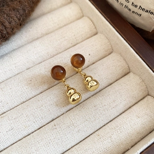 Detail of vintage tiger eye hulu earrings with gold relief pattern on white velvet