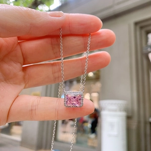 Close-up of square cut pink zircon pendant with silver chain held by hand outdoors