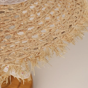 Detail view of woven raffia sun hat with delicate lace trim and fringed edges