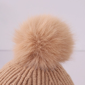 Macro detail of thick beige ribbed knit beanie featuring a large faux fur pom-pom topper