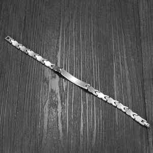 Minimalist silver stainless steel fish-shaped bracelet on dark wood background