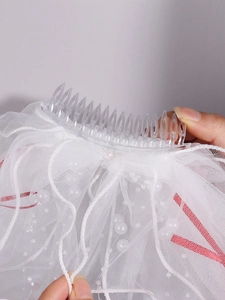 Detail of multi-layer white bridal veil with pearl accents and clear hair comb attachment