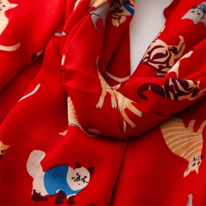 Detail of red scarf featuring colorful cartoon cat patterns and soft woven texture