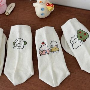 Detailed view of four white cotton socks with cute cartoon embroidery on a wooden table