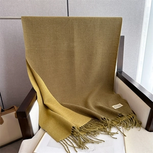 Detail of soft mustard yellow and dark green cashmere-like scarf with fringe on a chair