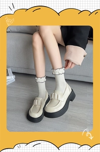 Detail of cream platform loafers with white ruffled socks and a decorative bow tie