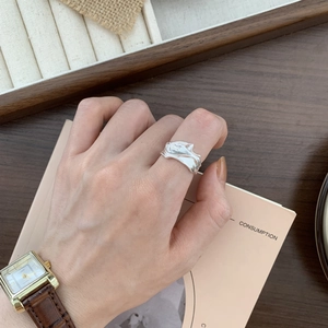 Detailed view of silver liquid metal texture ring worn on a model hand with vintage props
