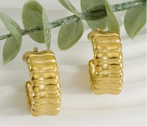 Close-up of chunky gold-plated U-shaped ribbed hoop earrings on a minimalist background