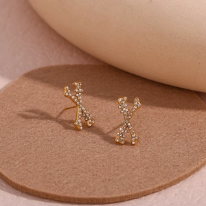 Detail of gold X-shaped stud earrings with pave-set zircon crystals on a soft background