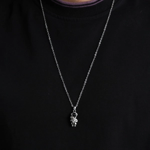 Close-up of silver astronaut pendant on O-chain necklace worn over black knit sweater