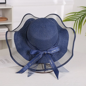 Detail of dark blue straw sun hat featuring wave organza brim and bow with gold lettering