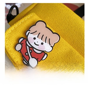 Close-up of a cute cartoon enamel pin attached to a yellow canvas crossbody messenger bag