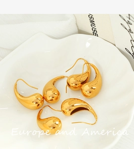 Close-up of golden teardrop earrings with mirror polish finish on a white shell tray