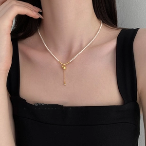 Détail d'un collier de perles blanches avec pendentif gourde dorée et fines chaînes pompon