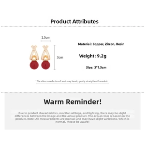 Detail view of gold-plated cross earrings with zircon and a hanging red resin bead