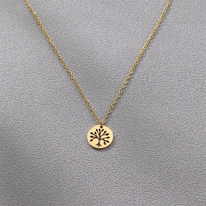 Detailed flat lay of a golden stainless steel tree of life pendant on a grey surface