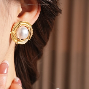 Close-up of pearl earrings with golden spiral base worn by a model in warm light