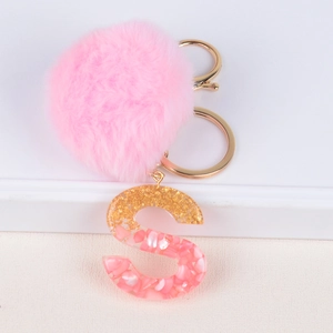 Close-up of pink pompom and gold foil resin letter S keychain on white background