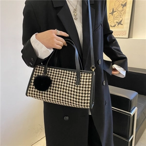 Detail of houndstooth handbag featuring black leather handles and a fuzzy pom-pom charm