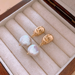 Détail de boucles d'oreilles vintage en métal doré visage avec perles baroques blanches