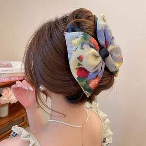 Detailed view of an oil painting style floral bow hair clip on a brunette bun hairstyle