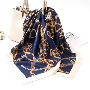 Detail of luxury navy silk scarf with gold chain print tied on a white handbag handle