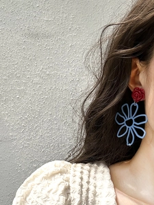 Detail view of red resin rose and blue hollowed floral earrings worn by a model