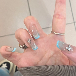 Gros plan sur ongles press-on bleus style français avec papillons argentés et strass