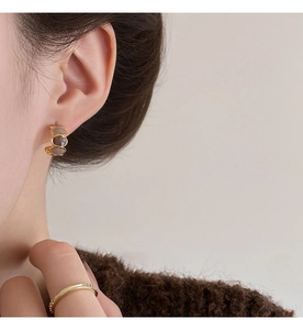 Close-up of three-tier golden C-shaped earrings with dark brown enamel on model