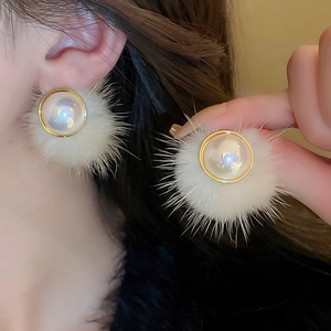 Detail of elegant white faux fur pompom earrings with a centered pearl and gold rim