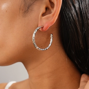 Close-up of a textured silver C-shaped geometric hoop earring worn by a model