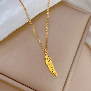 Gros plan détaillé d'un collier avec pendentif plume dorée dans un écrin à bijoux beige