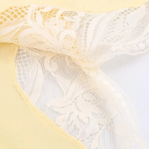 Close-up of yellow plain fabric with intricate white lace floral embroidery detail