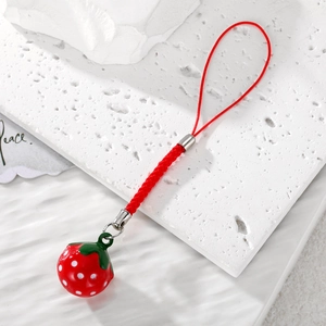 Detail of red strawberry bell pendant with woven lanyard on a white textured background