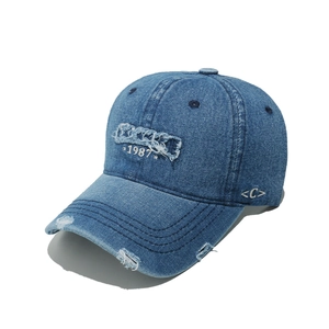 Close-up of distressed denim baseball cap featuring 1987 embroidery and vintage ripped details