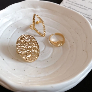 Macro detail of three gold-finished hammered and geometric rings on a ceramic plate