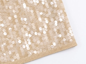 Detailed close-up of champagne gold sequin fabric with intricate knit texture and shine