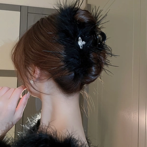 Detail of a black feather hair claw clip featuring a sparkling rhinestone planet charm