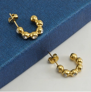 Detail of 18K gold-plated U-shaped earrings with sparkling cubic zirconia on blue base