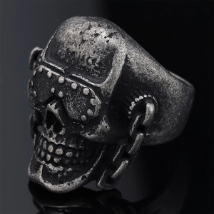 Retro gothic skull ring with goggles and chain detail on a black reflective surface