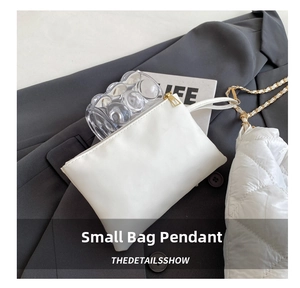 Dettaglio di ciondolo per borsa in pelle bianca con zip dorata su sfondo di abito grigio
