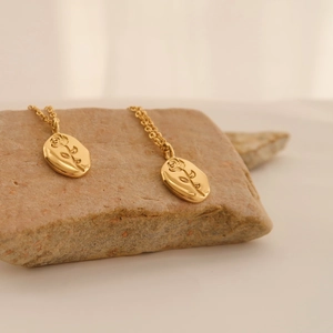 Macro shot of rose flower engraved oval pendants on gold stainless steel chains