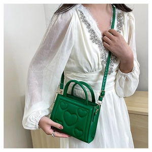 Gros plan d'un sac bandoulière vert en cuir PU avec motifs de cœurs en relief et poignée