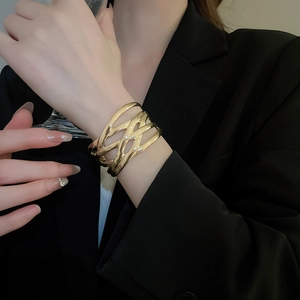 Detailed view of wide gold intertwined woven bracelet worn on black sleeve