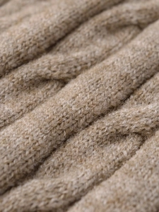 Macro shot of chunky cable knit texture in beige, highlighting warm wool material fibers