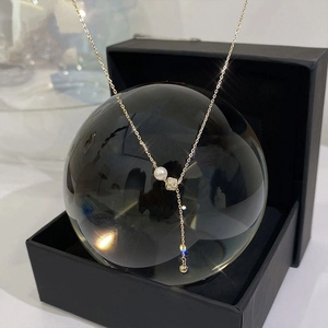 Detail of Y-shaped gold pearl necklace with zircon beads displayed on a crystal sphere