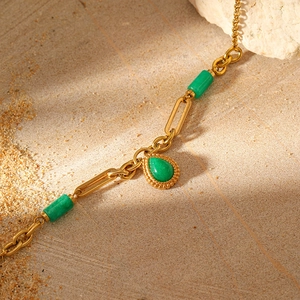 Macro detail of gold-plated chain bracelet featuring green teardrop gemstone and beads